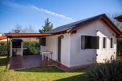 a small white house with a wooden deck at Cabañas Montecarlo 3 in Santa Rosa de Calamuchita