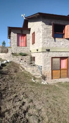 a stone house with brown doors and a yard at El Alma De Yacanto Hotel Boutique in Villa Yacanto