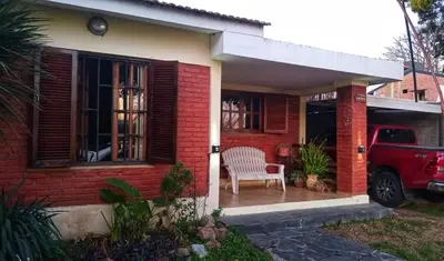 a red brick house with a chair on a porch at Cómoda y Espaciosa Casa Céntrica Frente al Lago San Roque - Carlos Paz in Villa Carlos Paz