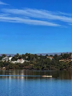 a boat on a lake with a town in the background at Cómoda y Espaciosa Casa Céntrica Frente al Lago San Roque - Carlos Paz in Villa Carlos Paz