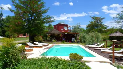 a swimming pool with lounge chairs and a red house at Puesto Potrillos in Villa Yacanto