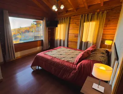a bedroom with a red bed in a wooden room at Cuesta de las Piedras in La Cumbrecita