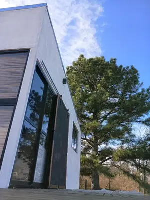 a white building with a large window next to a tree at Kururu Cabaña en Villa Yacanto con vista a las sierras in Villa Yacanto