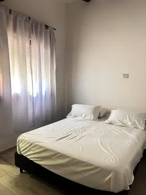 a bed with white sheets and pillows next to a window at Cabañas Antartida in Villa Carlos Paz