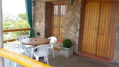 a wooden table and white chairs on a porch at Cabaña Punta Piedras in Villa Carlos Paz