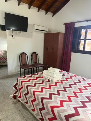 a bedroom with a bed and two chairs and a tv at Cabañas Costa Alta in Mina Clavero