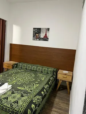 a bedroom with a bed with a green comforter and a table at Hospedaje Malvinas in Alta Gracia