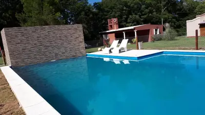 a large blue swimming pool with two white chairs in it at La Casona Cabañas in Villa Ciudad Parque