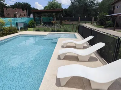 a swimming pool with two white chairs next to it at Departamentos Pura Fe in Santa Rosa de Calamuchita