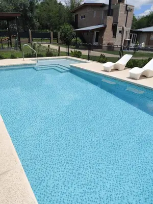 a large blue swimming pool with two white chairs at Departamentos Pura Fe in Santa Rosa de Calamuchita