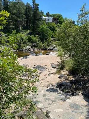 a river with rocks and trees and a house in the background at Brisas Serranas in Villa Icho Cruz