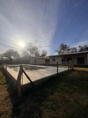 a fence in front of a house with the sun behind it at Entre Algarrobos - Cabañas con pileta y naturaleza in Villa de Las Rosas