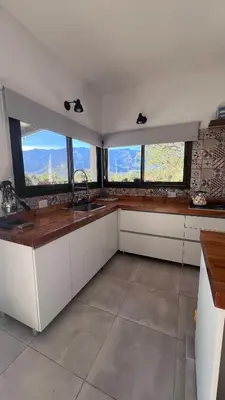 a kitchen with white cabinets and windows with mountains at Sol & Río Refugio Serrano in Villa de Las Rosas