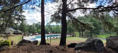 a swimming pool in a park with trees and rocks at Aldea de los Cerros in Villa Yacanto