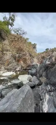 a river with rocks and trees on a hill at Cabañas Yarel in Alpa Corral