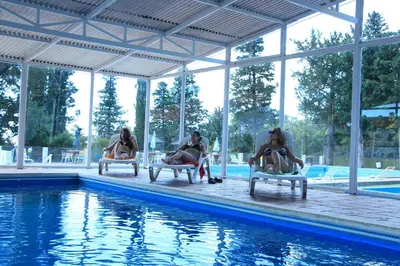 three people sitting in chairs next to a swimming pool at El Condor Hotel SPA in Merlo