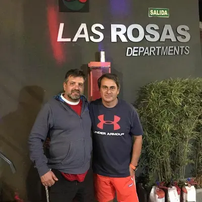 two men standing next to each other in front of a sign at La Rosas apartments in La Porteña