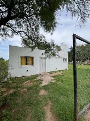 a white house in a field with a fence at cabaña con pileta in Villa Anizacate