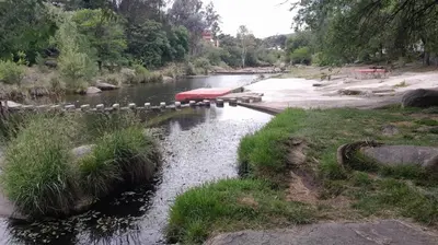 a river with rocks and grass and a bridge at Departamento en Villa del Lago, Carlos Paz in Villa Carlos Paz