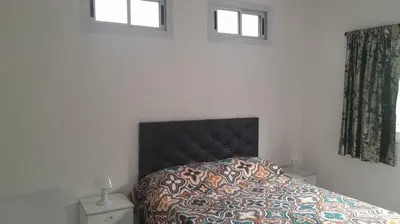 a bedroom with a bed with a black headboard and two windows at Departamento en Villa del Lago, Carlos Paz in Villa Carlos Paz