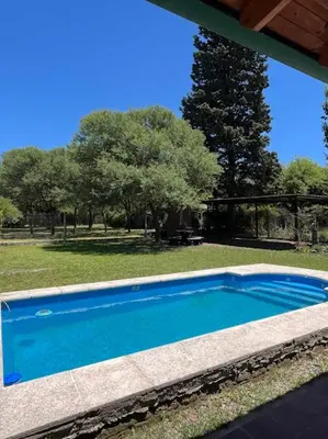 a blue swimming pool in a yard with trees at Cabañas El Chañar in Villa Santa Cruz del Lago