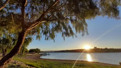 a tree in front of a lake with the sunset at Duplex Villa Carlos Paz in Villa Carlos Paz