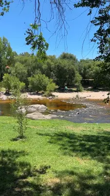 a river with trees and a grassy field next to a river at Lodemarta in Villa Carlos Paz
