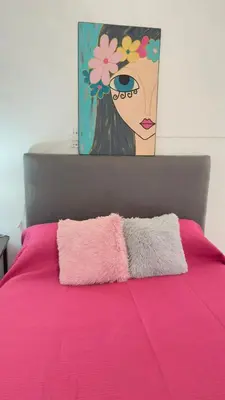 a bed with pink sheets and a painting of a woman at Habitación con baño zona cucú 2 personas in Villa Carlos Paz