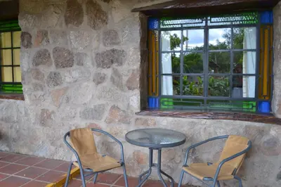 two chairs and a table in front of a stone wall at Rumi Huasi Cabañas in Mina Clavero