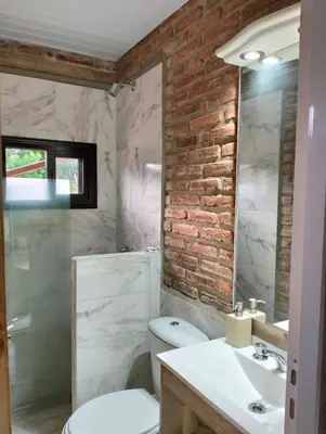 a bathroom with a white toilet and a brick wall at Panorámica Sierras in Villa Carlos Paz
