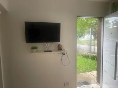 a flat screen tv on a wall with a window at Jardín del norte a mts de sanatorio Allende, Hospital Privado cerro,Nascentis y estadio Kempes in Cordoba