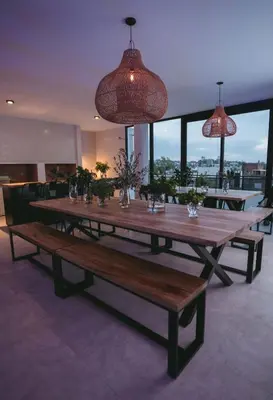 a large wooden table with benches in a room with windows at Departamento moderno pleno centro con pileta y cochera privada in Villa Carlos Paz