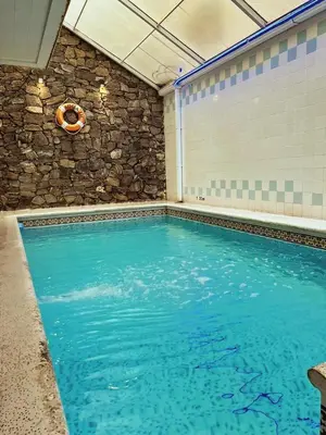 an indoor swimming pool with a stone wall and blue water at Gran Lourdes Hotel in Villa Carlos Paz
