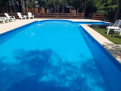 a blue swimming pool with white chairs and tables at Hosteria Arture in Villa Cura Brochero