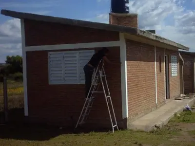 a man standing on a ladder in front of a house at Sierras y sol in Villa Cura Brochero