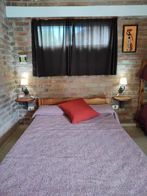 a bedroom with a brick wall and a bed with a red pillow at Cabañas del IntiCo in Arroyo de Los Patos