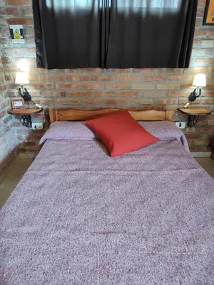 a bed with a red pillow and a brick wall at Cabañas del IntiCo in Arroyo de Los Patos