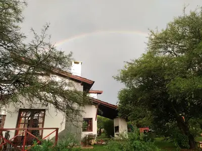a rainbow over a white house with trees at Cabañas Rey Garcia in Villa General Belgrano