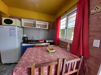 a kitchen with a table and a refrigerator and red curtains at Departamentos Las Marias in Villa Cura Brochero