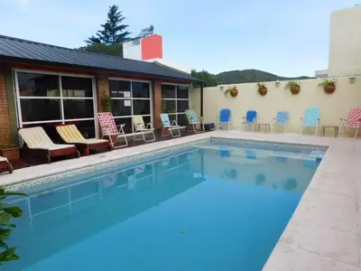 a swimming pool with chairs and a building at Complejo Carola in Villa Carlos Paz