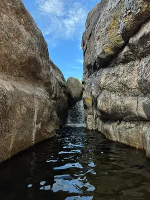 a waterfall between two large rocks in a pool of water at Cabaña El Molle - Los Nogales in Mina Clavero