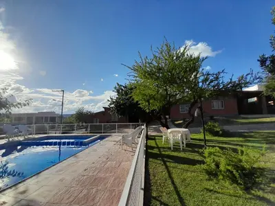 a swimming pool with two white chairs and a tree at Cabañas Nuestro Valle Cura Brochero in Villa Cura Brochero