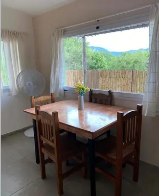 a dining room table with chairs and a large window at Casitas Rabe in Santa Rosa de Calamuchita