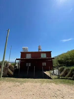 a red building sitting on top of a dirt field at Cabañas El Pela in Villa Carlos Paz