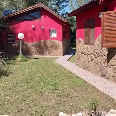 a red house with a stone wall next to a yard at Casas de alquiler villa ciudad parque in Villa Ciudad Parque