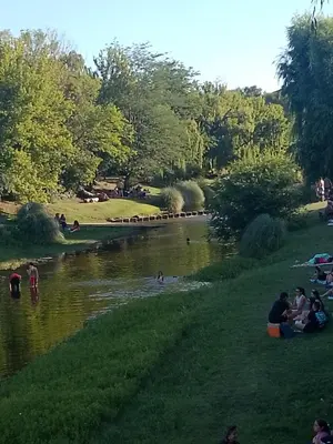 a group of people sitting on the grass by a river at La tranquera in Trapiche