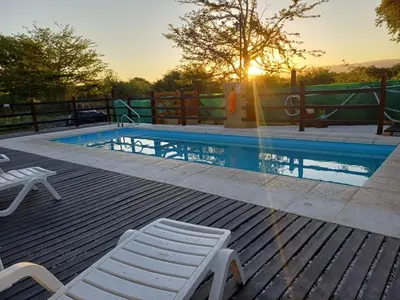 a swimming pool with two white chairs and the sunset at DoñaMaria in Santa Rosa de Calamuchita