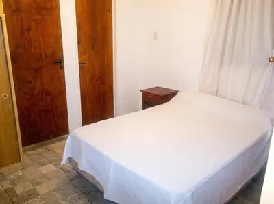 a bedroom with a white bed and a wooden door at Brisas Serranas Departamentos in Villa Carlos Paz