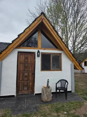 a cabin with a wooden door and a chair and a tree stump at Cabañas Gran Aldea in Mina Clavero