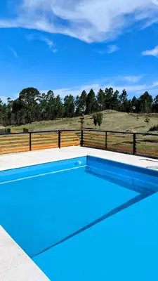 a blue swimming pool with a fence and a field at La Insolente in Villa Yacanto